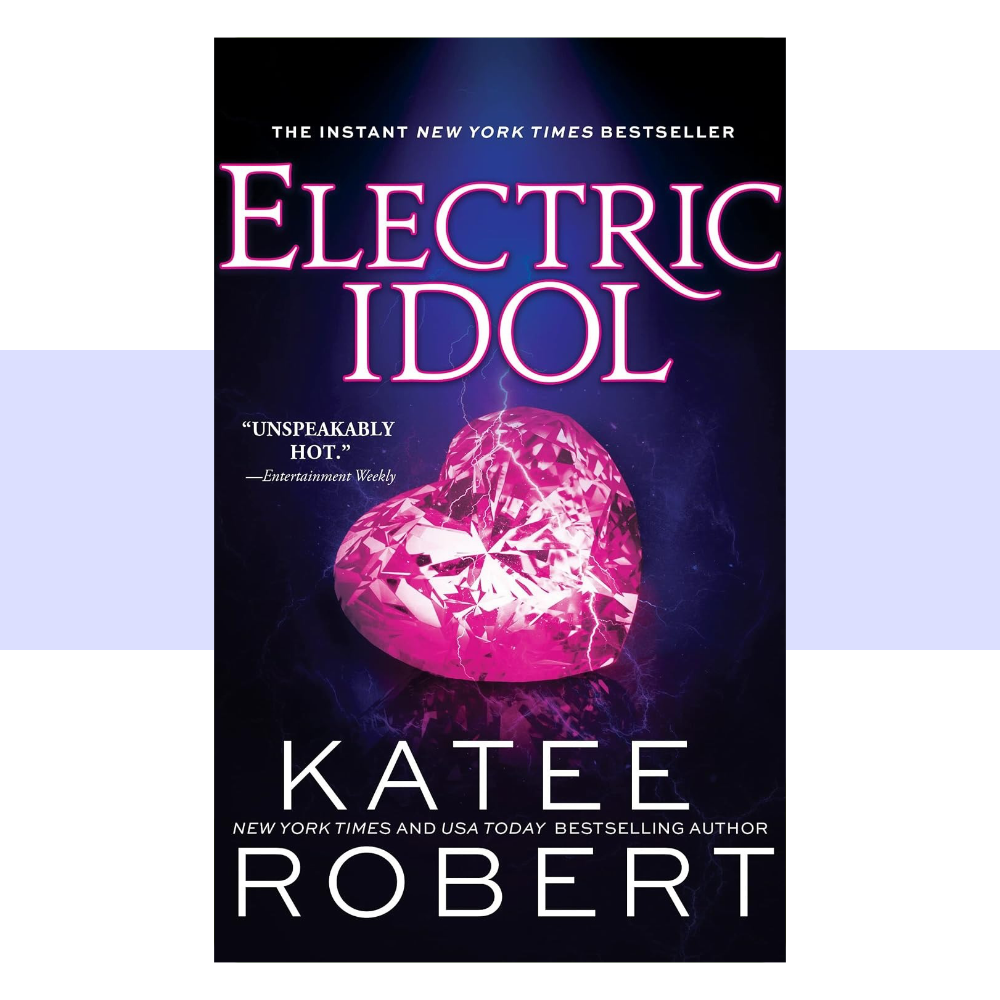 Book cover for Electric Idol by Katee Robert. The cover features a dark, nearly black background with rich electric blue and deep purple tones creating a dramatic, luxurious atmosphere. A large, luminous blue heart-shaped gemstone or crystal dominates the center of the design, surrounded by delicate metallic-looking elements and subtle decorative details. The title “ELECTRIC IDOL” appears prominently across the upper portion in large, elegant white serif lettering, with “DARK OLYMPUS” in smaller white text